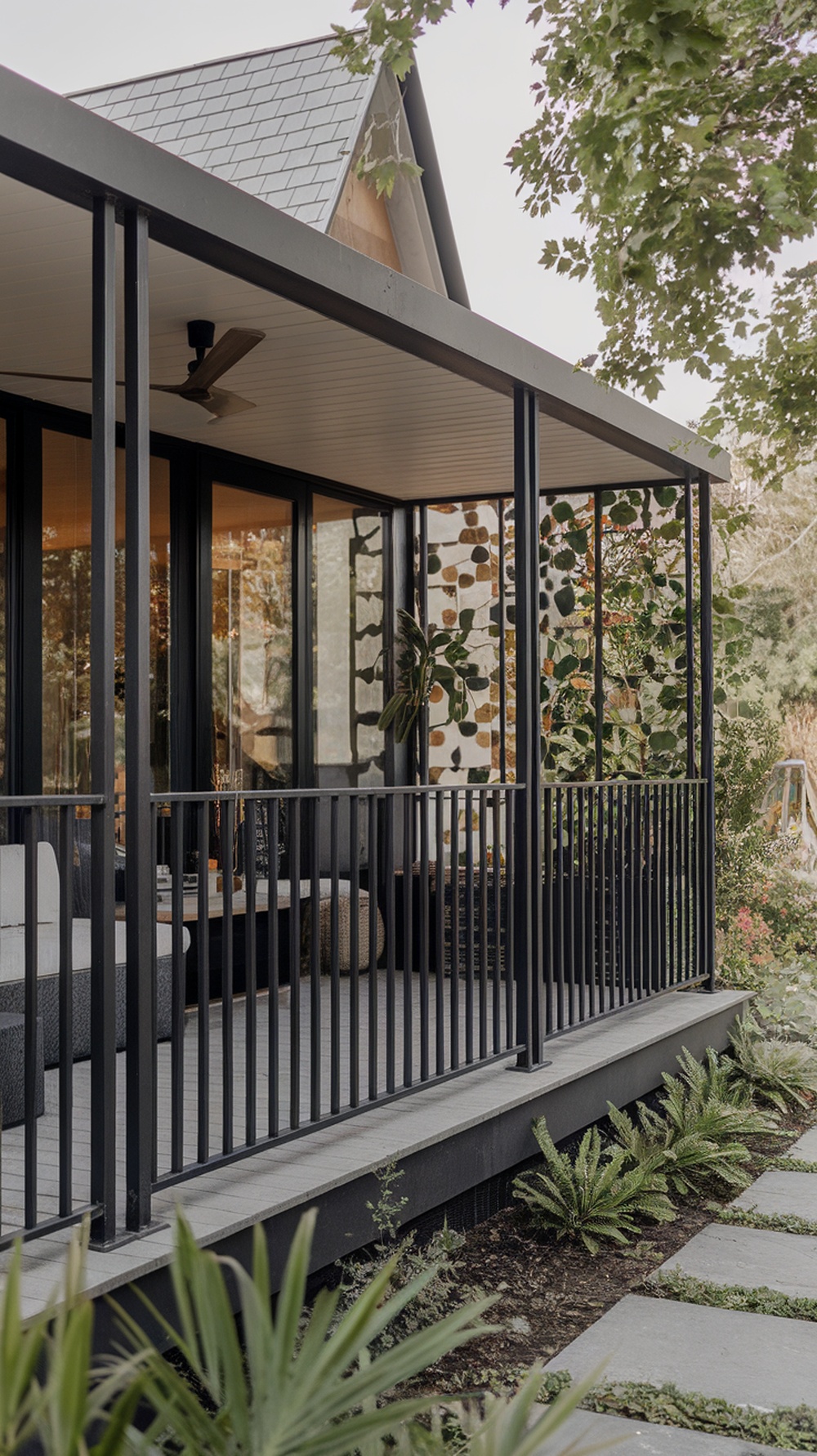 A modern porch featuring sleek black metal railings, surrounded by greenery.