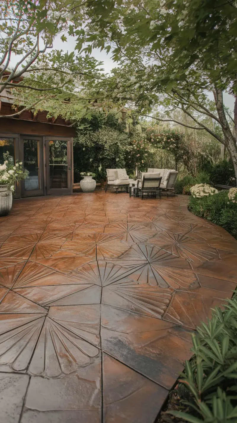 A beautifully designed stamped concrete patio with a fan pattern in rich brown tones, surrounded by greenery and outdoor furniture.