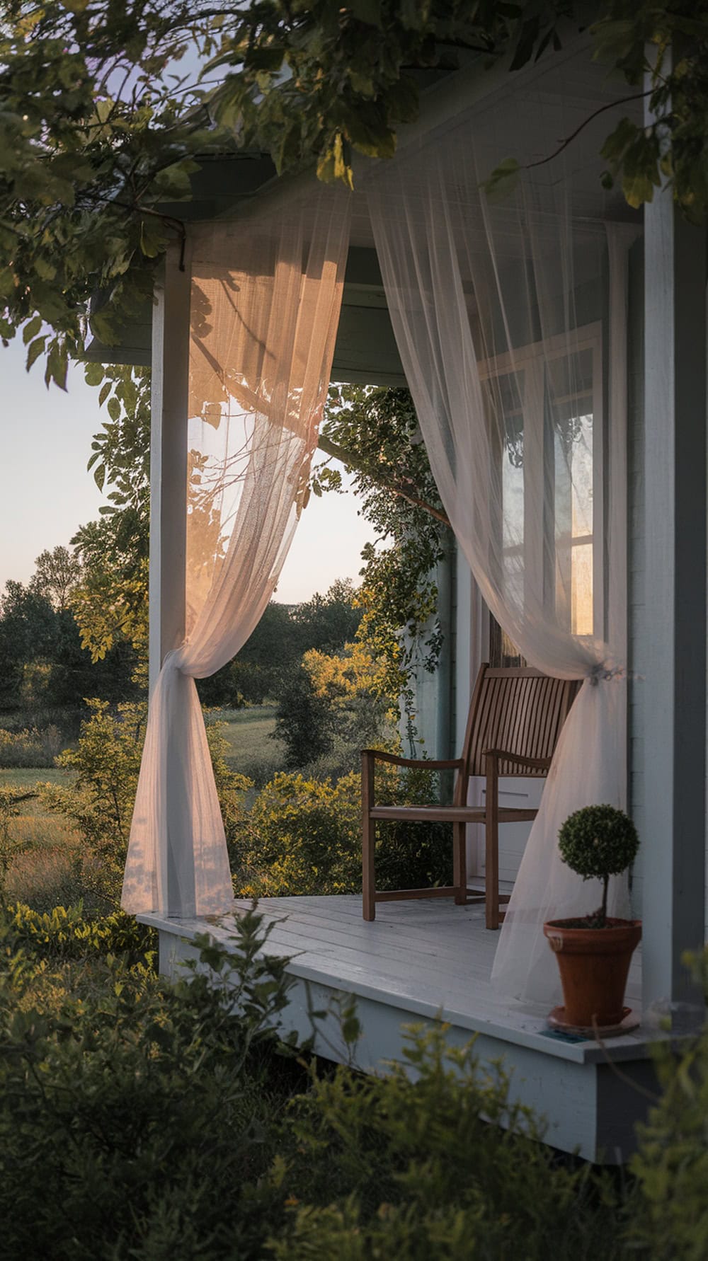 A porch with mosquito netting curtains, a wooden chair, and a small potted plant.