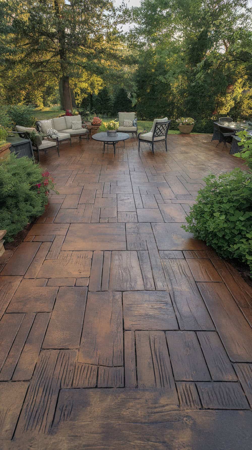 A rustic wood plank stamped concrete patio surrounded by greenery and outdoor furniture.